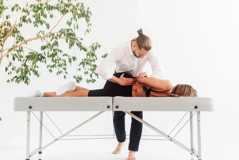 Fizjoterapeuta z Uzdrovisko wykonuje terapię manualną kręgosłupa u pacjentki leżącej na boku na stole do terapii.