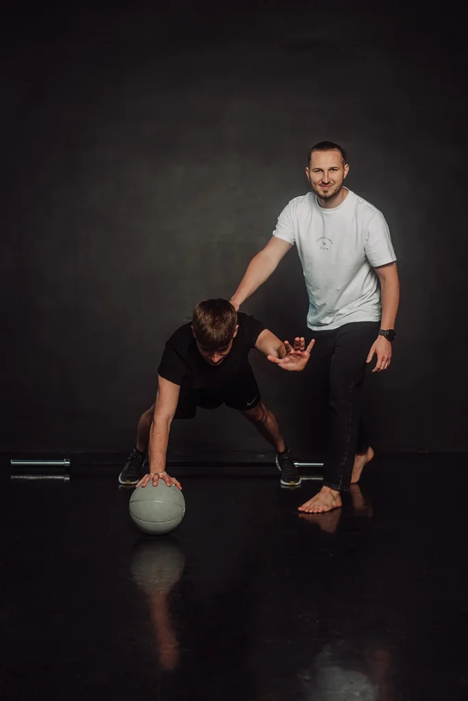 Trening medyczny w Uzdrovisko – fizjoterapeuta koryguje postawę pacjenta podczas ćwiczenia stabilizacyjnego z piłką.